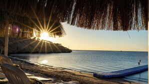 A beach scene with a thatched roof structure, a rocky coastline, and a calm sea. - Continental Plaza Beach Resort (Sharm El Sheikh)