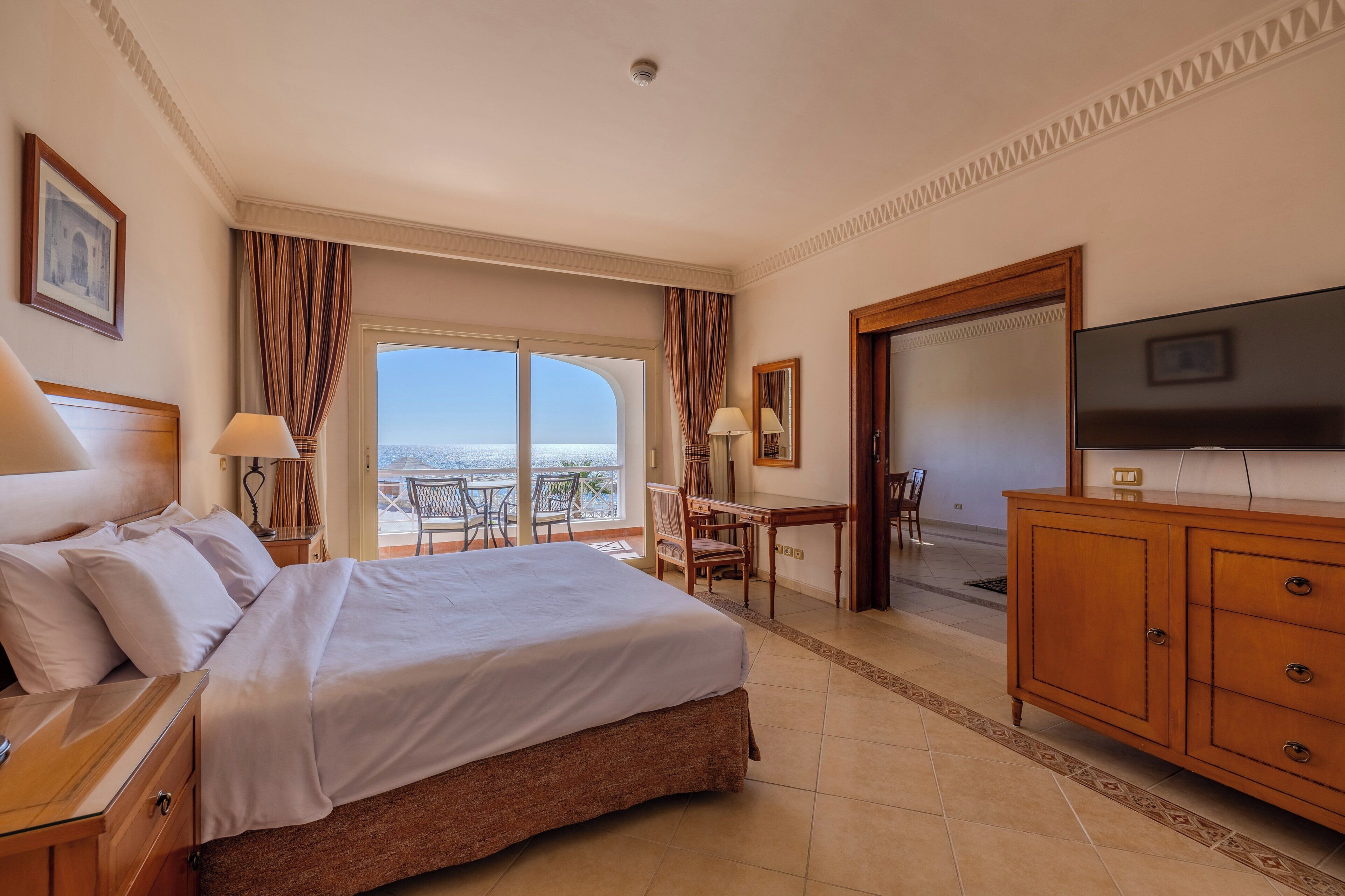 A hotel room with a large bed, a TV, a desk, and a balcony with a view.