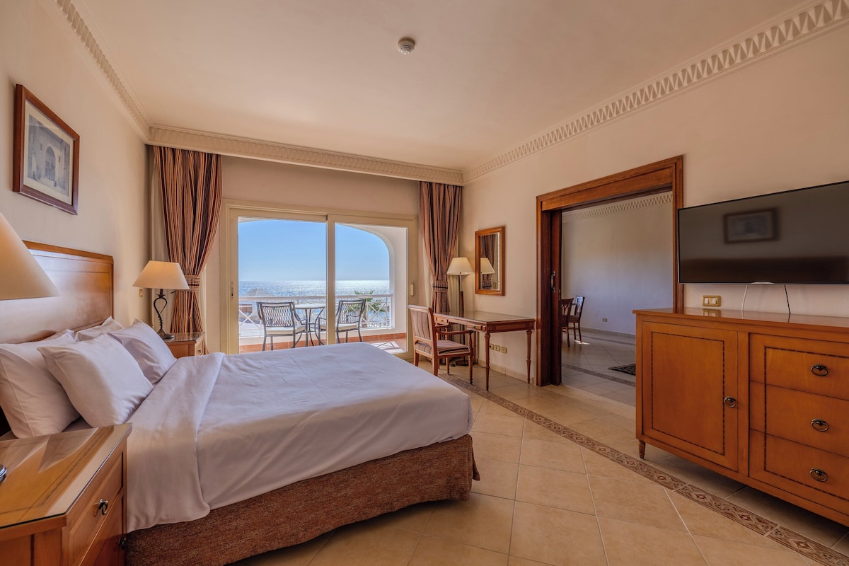 Habitación de hotel con una cama grande, televisión, escritorio y balcón con vistas.