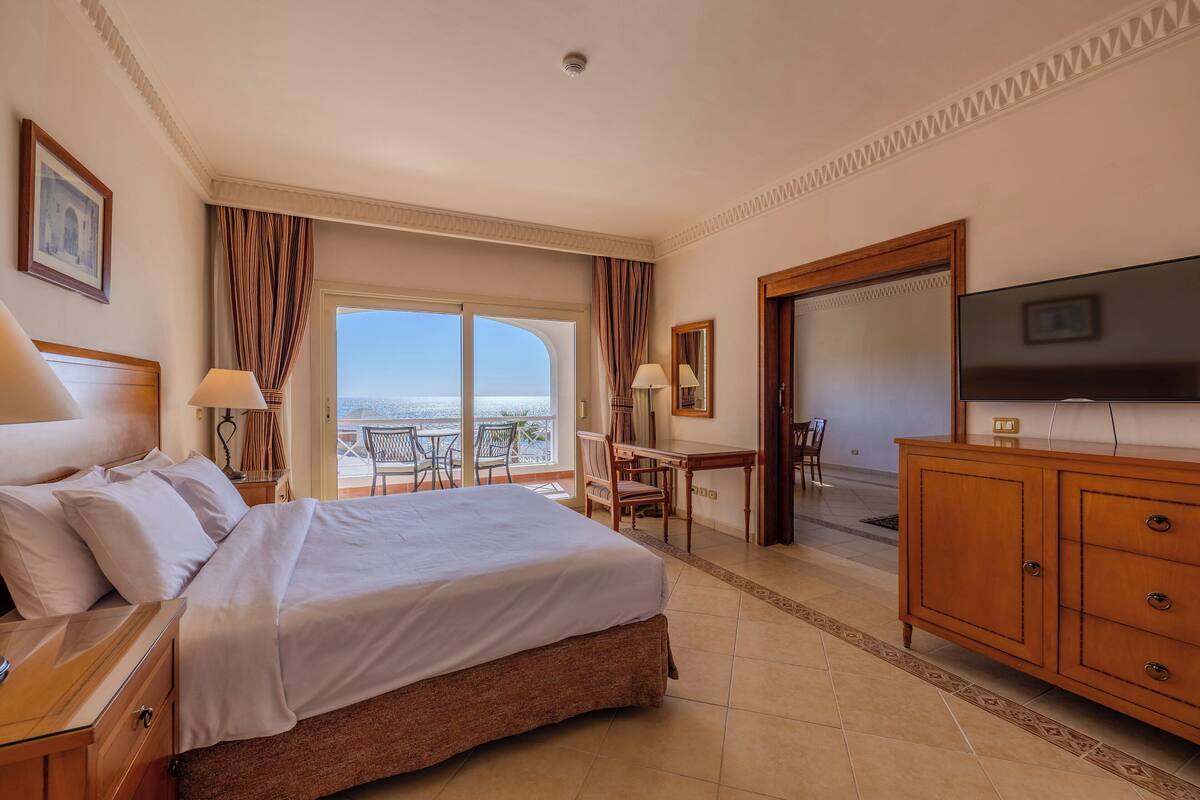 Habitación de hotel con una cama grande, televisión, escritorio y balcón con vistas.