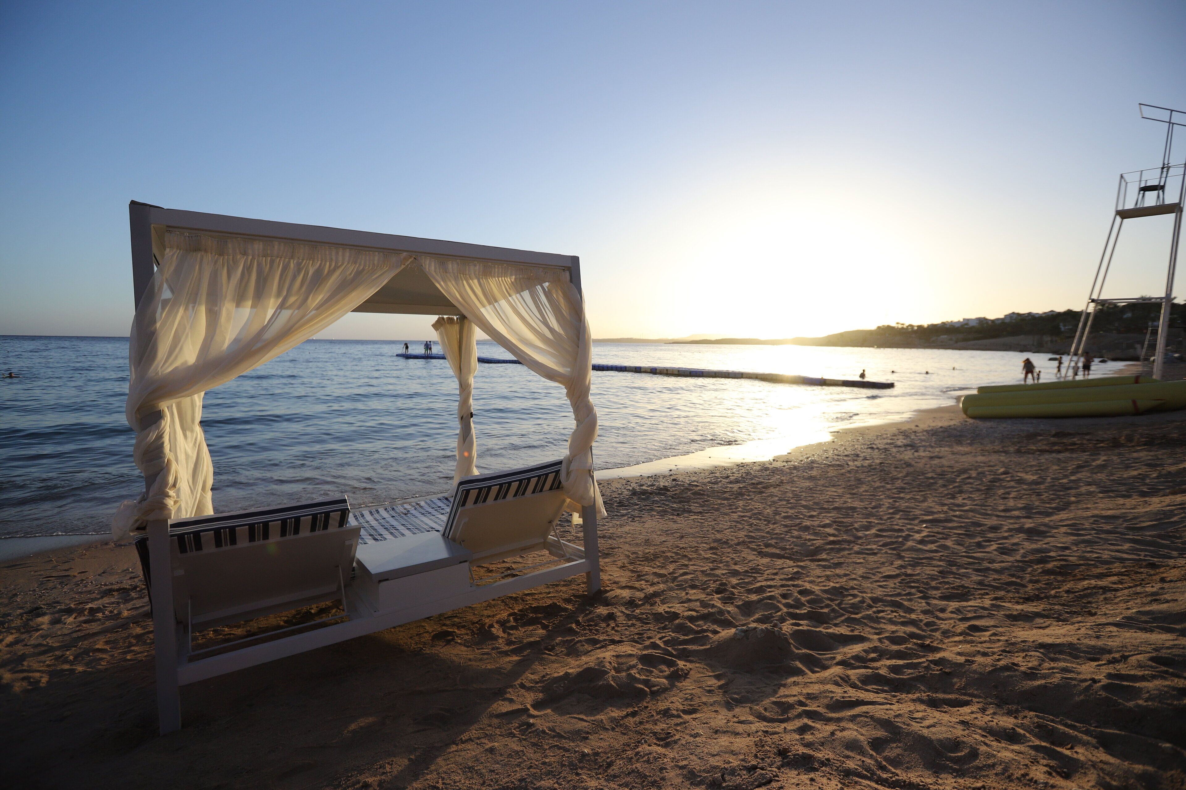 Une plage avec un lit à baldaquin blanc et un poste de surveillance pour les sauveteurs.