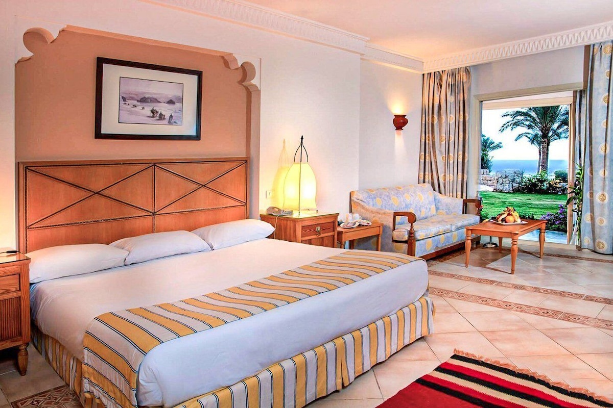 Habitación de hotel con una cama grande, un sofá, un escritorio, una lámpara y vistas al océano.