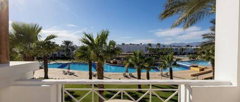 A poolside view with a clear sky, palm trees, and a pool.