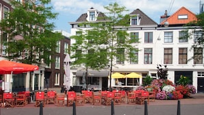 A street with outdoor seating, a flower bed, and buildings with red-tiled roofs. - Short Stay Maff Apartment (The Hague)
