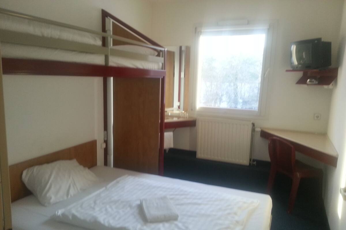 A hotel room with bunk beds, a desk, a chair, a television, and a window with a view.