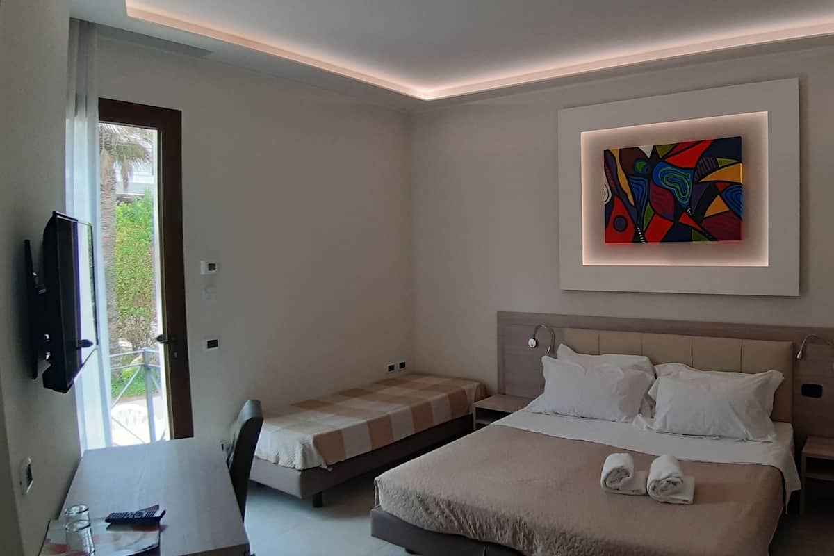 Habitación de hotel moderna con una cama grande, una cama más pequeña, un televisor y un cuadro en la pared.