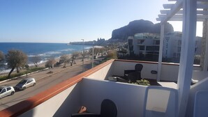 A balcony with a view of the sea, a road with parked cars, and modern buildings in the background. - Villa Cerniglia (Cefalù)