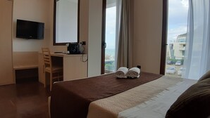 A hotel room with a bed, a desk with a chair, a television, and a window with curtains. - Villa Cerniglia (Cefalù)