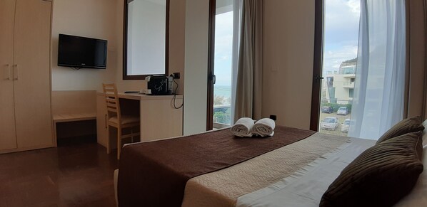 Habitación de hotel con cama, escritorio con silla, televisor y ventana con cortinas.