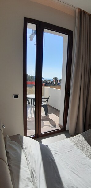 A hotel room with a bed, a window with curtains, and a view of a balcony with outdoor furniture. - Villa Cerniglia (Cefalù)