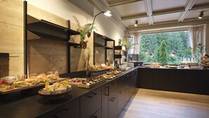 A modern kitchen with a long counter displaying various food items and a large window offering a view of the outdoors. - Bonfanti Design Hotel (Chienes)