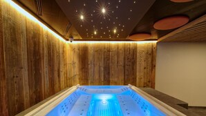 A modern spa room with a wooden wall, a blue-lit hot tub, and a starry ceiling. - Bonfanti Design Hotel (Chienes)