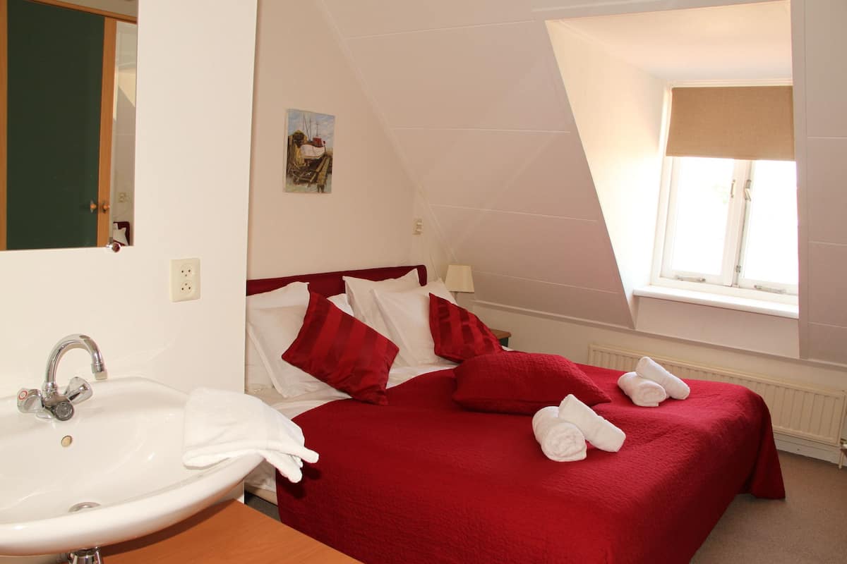 A hotel room with a bed, red bedding, a white sink, and a window with a view.