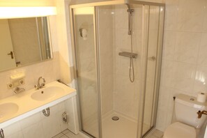 A bathroom with a glass-enclosed shower, a double sink, and a toilet. - Hotel De Korenbeurs-Willem4 (Kortgene)