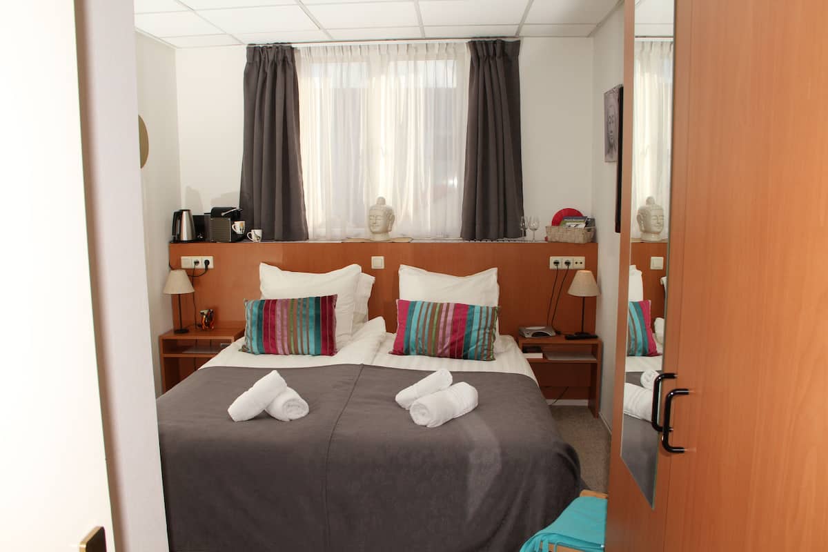 A hotel room with a bed, bedside tables, a window with curtains, and a mirror on the door.