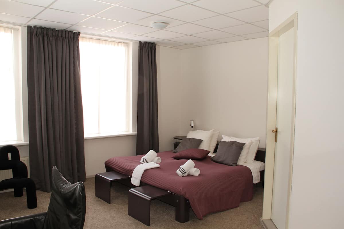 A hotel room with a bed, a chair, a desk, and a window with curtains.