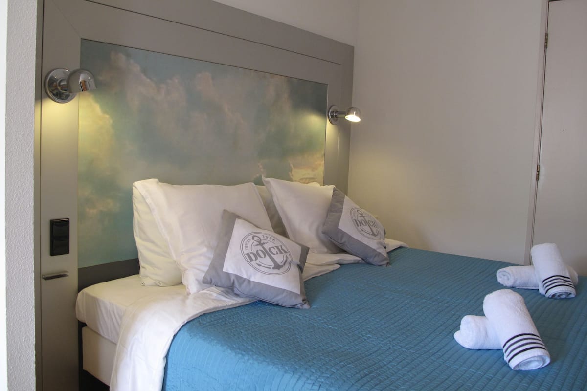 A hotel room with a bed, pillows, a blue bedspread, and a door.