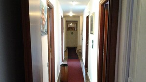 A narrow hallway with a red carpet, wooden doors, and a trash bin. - Hotel Massena (Genoa)