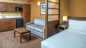 Una habitación de hotel con kitchenette, sofá, cama y mesita de noche con lámpara.
