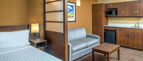 Habitación de hotel con cama, sofá, una mesita, microondas y lavamanos.
