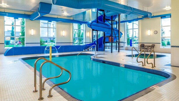 Una piscina interior con un tobogán azul, una zona de estar y vistas al exterior a través de amplios ventanales.
