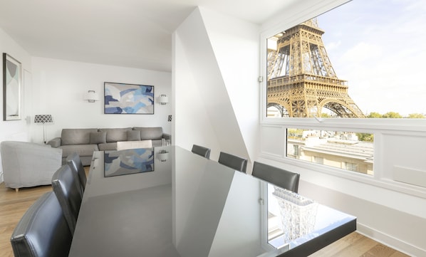 Un salon moderne avec un canapé, une table basse et une vue sur la Tour Eiffel, visible à travers une grande fenêtre.