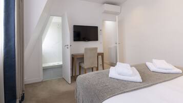 A hotel room with a bed, a desk, a chair, a television, and a shower.