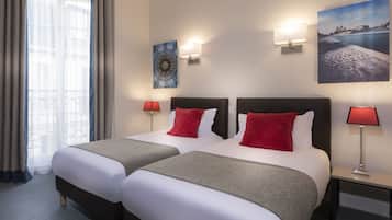 Une chambre d’hôtel avec deux lits, une table de chevet avec une lampe, un tableau au mur et une fenêtre avec des rideaux.