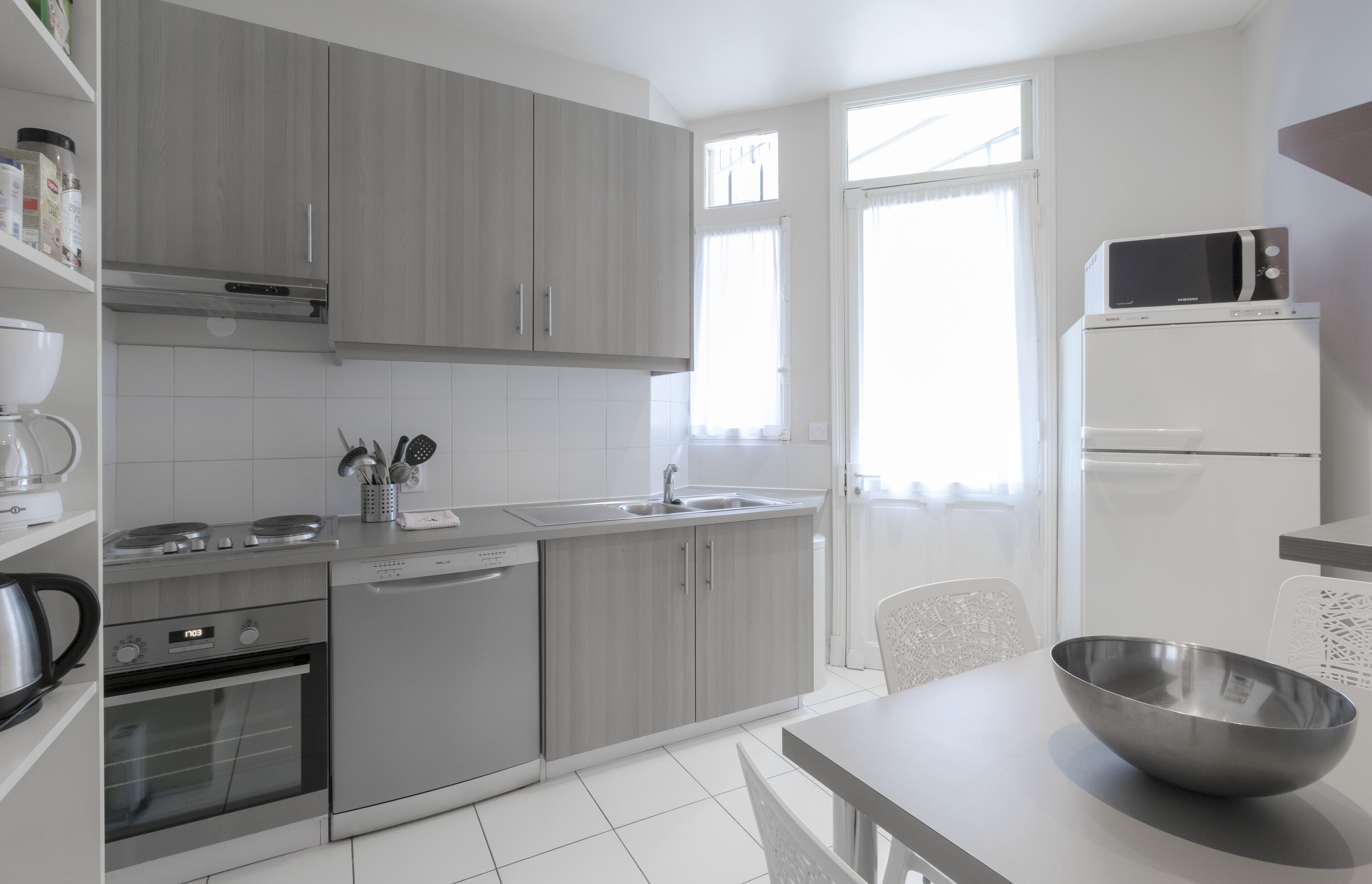 A modern kitchen with grey cabinets, a built-in oven, a microwave, and a sink.