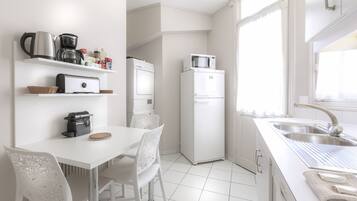 A modern kitchen with white appliances, a dining area with white chairs, and a large window providing natural light.