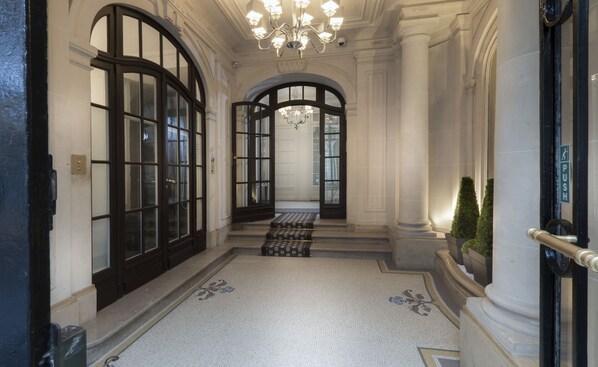 A grand hallway with large arched windows, a chandelier, and a patterned floor.
