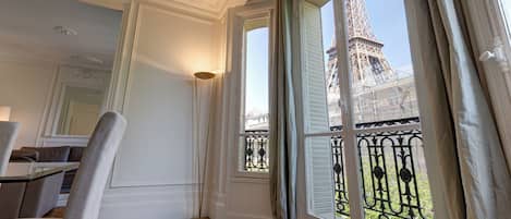 Quarto com vista para a Torre Eiffel, piso de madeira, uma cadeira e um abajur.
