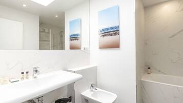 A modern bathroom with a large mirror, a white sink, a bidet, and two framed pictures on the wall.
