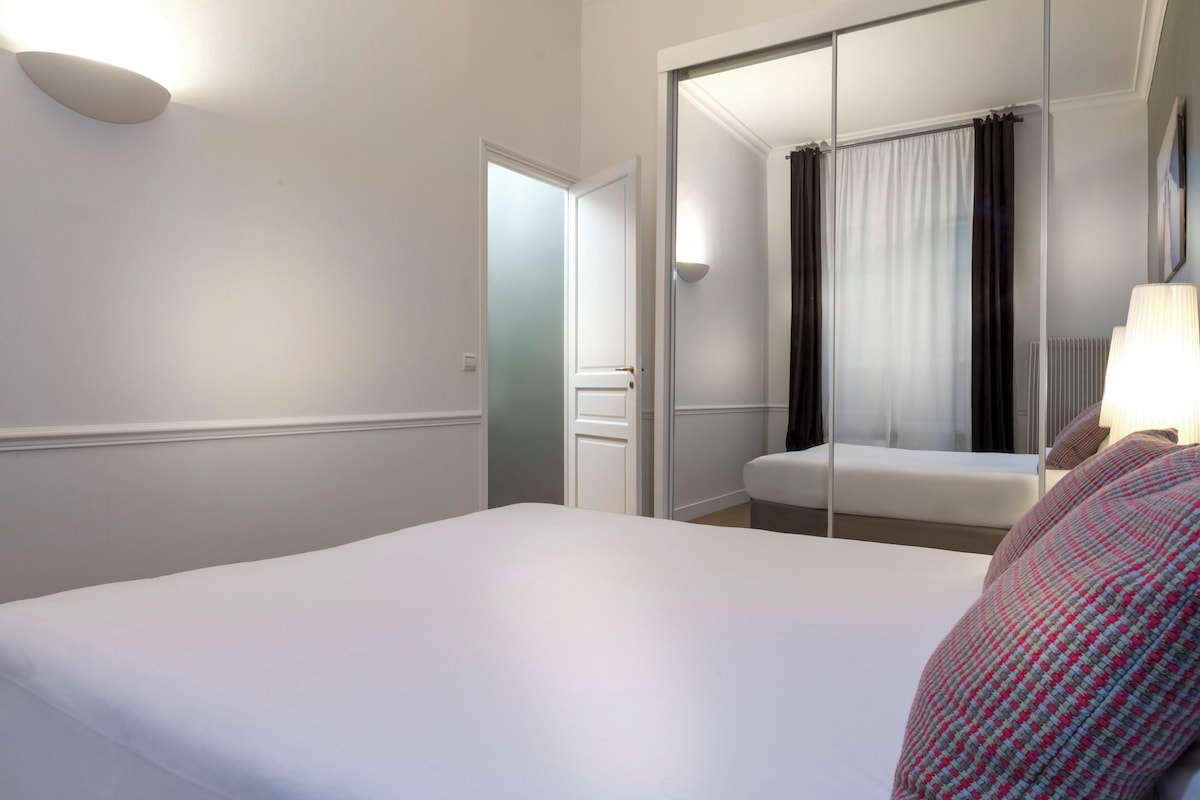 A hotel room with a large bed, a mirror, a wardrobe, and a bathroom with a shower curtain.