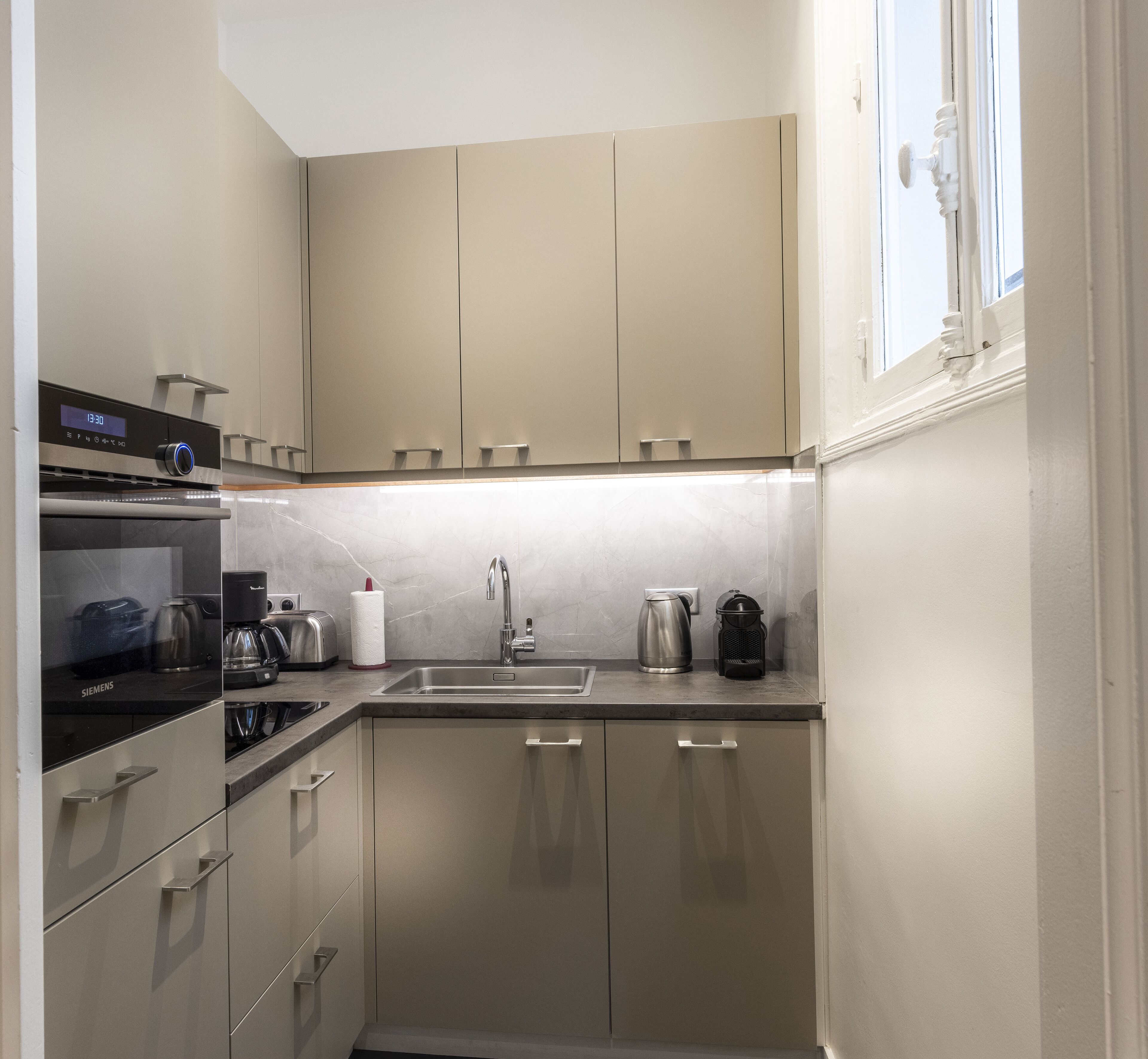 A compact kitchen with a built-in oven, a coffee maker, and a kettle on the countertop.