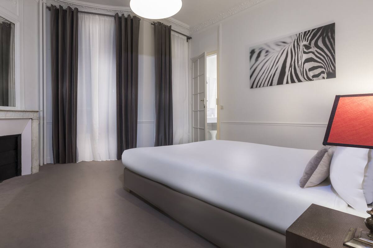A modern hotel room with a large bed, a fireplace, and a zebra print artwork on the wall.