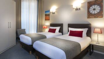 Une chambre d’hôtel avec deux lits, une armoire, une chaise, une table de chevet avec une lampe, et un mur orné d’un luminaire décoratif et d’un tableau encadré.