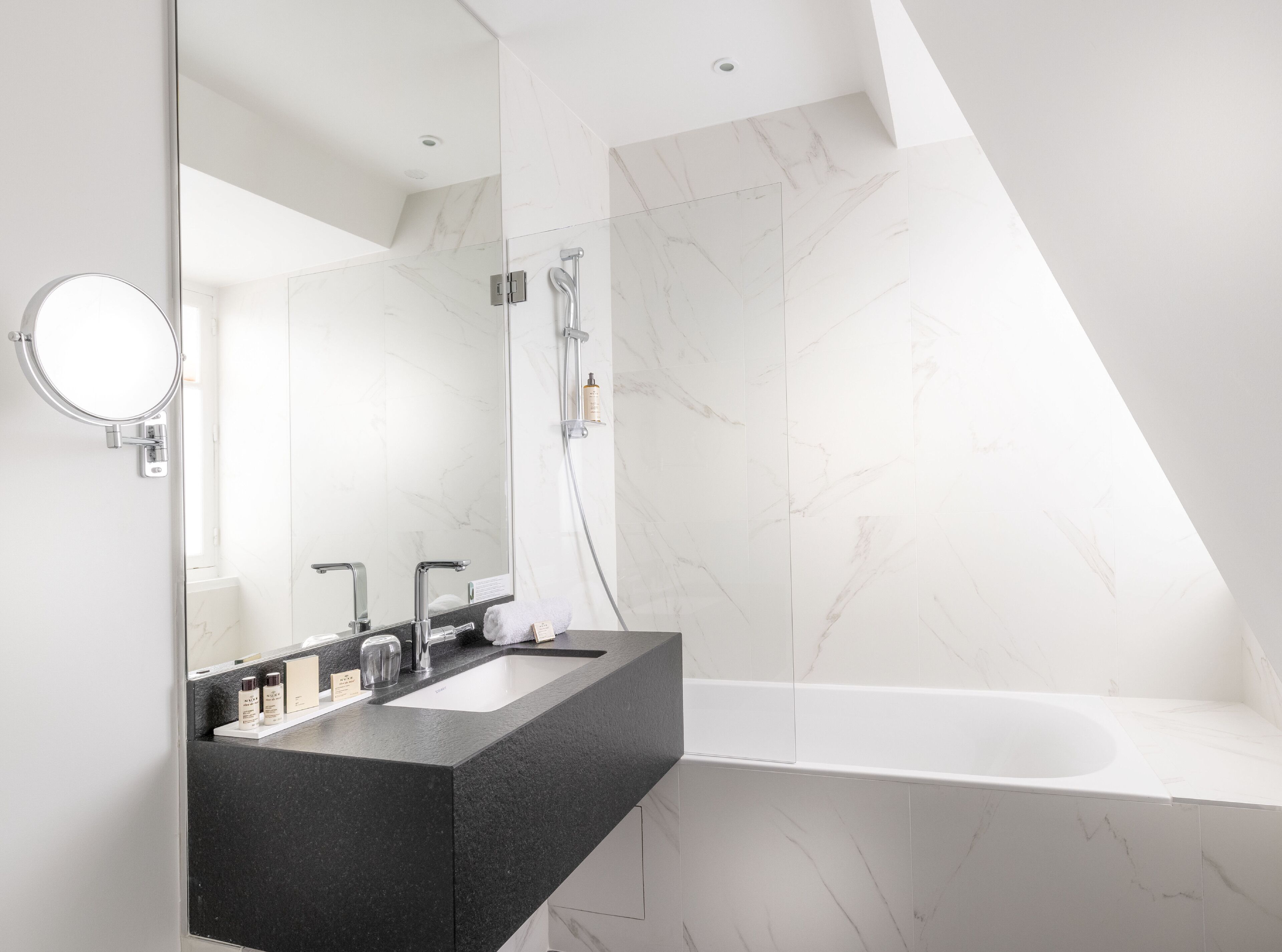 A modern bathroom with a dual sink vanity, a large mirror, a freestanding bathtub, and marble walls.