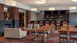 Vestíbulo de hotel con chimenea, zona de estar, bar y alfombra estampada.