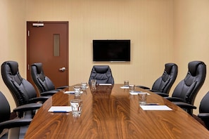 A conference room with a long wooden table, black leather chairs, a flat-screen TV on the wall, and a door. - Four Points By Sheraton Regina (Regina)