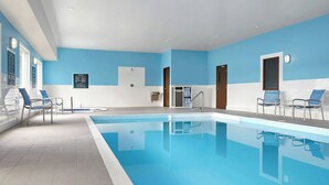 Una piscina con agua azul cristalina, rodeada de sillones de descanso y un suelo de baldosas.