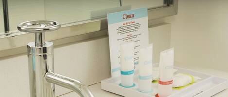 A bathroom with a chrome faucet, a sign that says "Clean," and a tray with three bottles of lotion and a bar of soap.