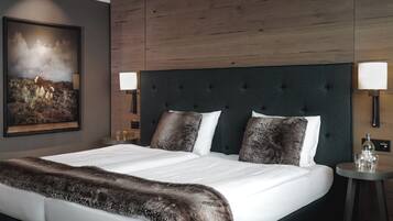 Habitación de hotel con una cama grande, cabecera, dos lámparas de noche, mesitas de noche, un cuadro enmarcado en la pared y una manta de piel sobre la cama.