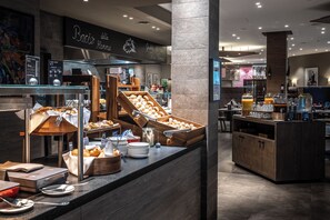 Un bufé de desayuno con diversos pasteles y pan, una estación de café y una zona de bar con bebidas.