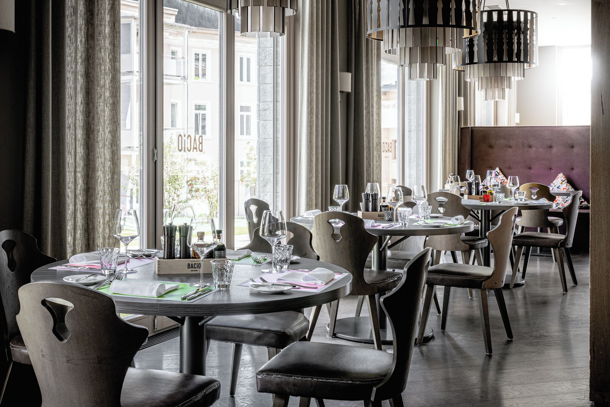 Um restaurante com mesas redondas, cadeiras e luminárias pendentes.