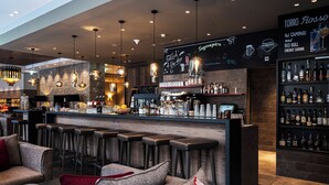 A bar area with stools, a counter, and shelves of bottles. - AMERON Davos Swiss Mountain Resort (Davos)