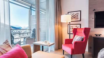 Una habitación de hotel moderna con un ventanal grande, un sillón rojo, una mesita y un televisor.