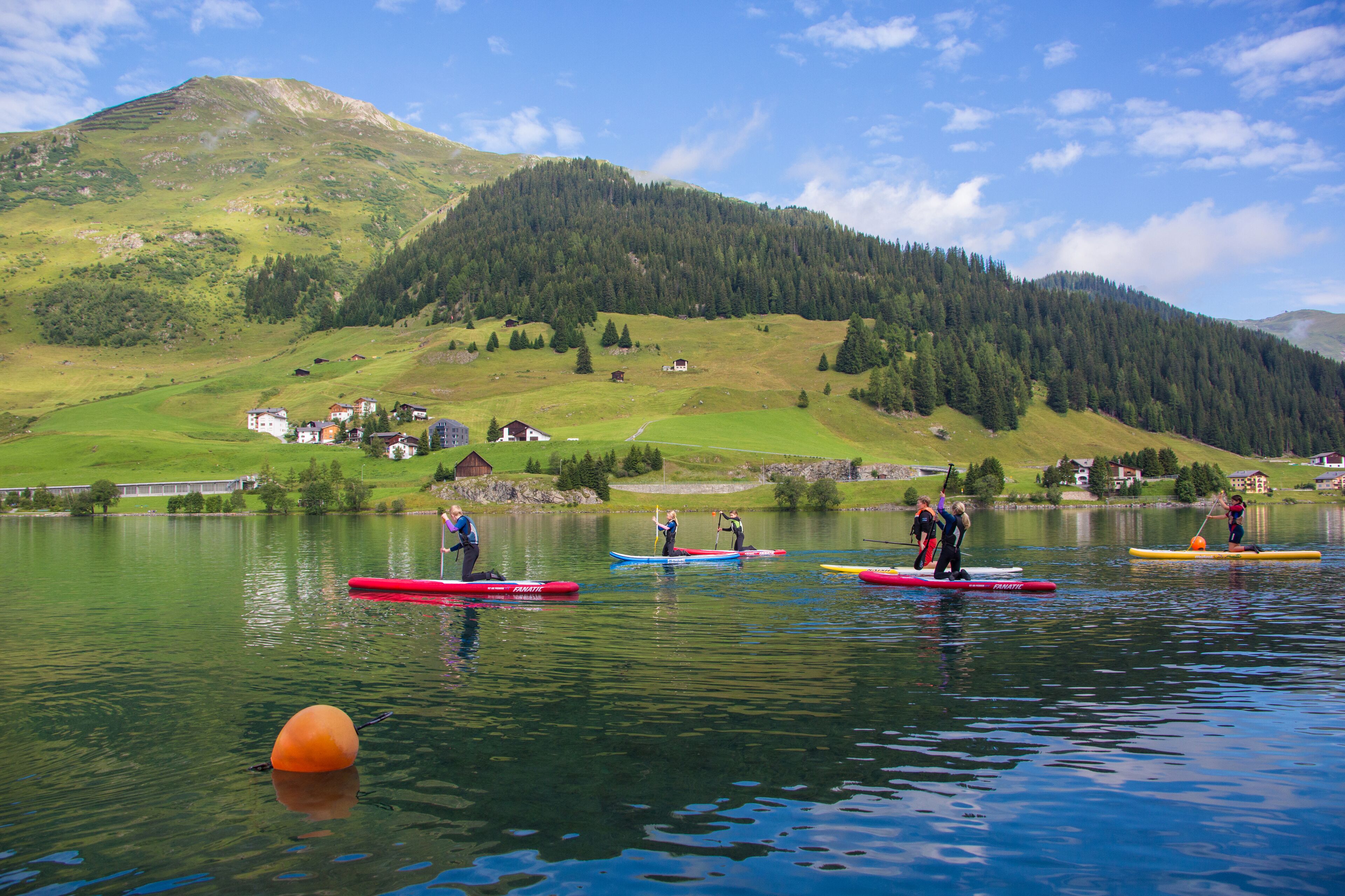 A group of people on paddleboards on a calm lake with a mountainous backdrop.