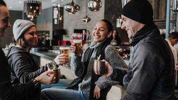 Un groupe de personnes est assis et trinque avec des boissons dans un cadre intérieur moderne, éclairé par des suspensions.