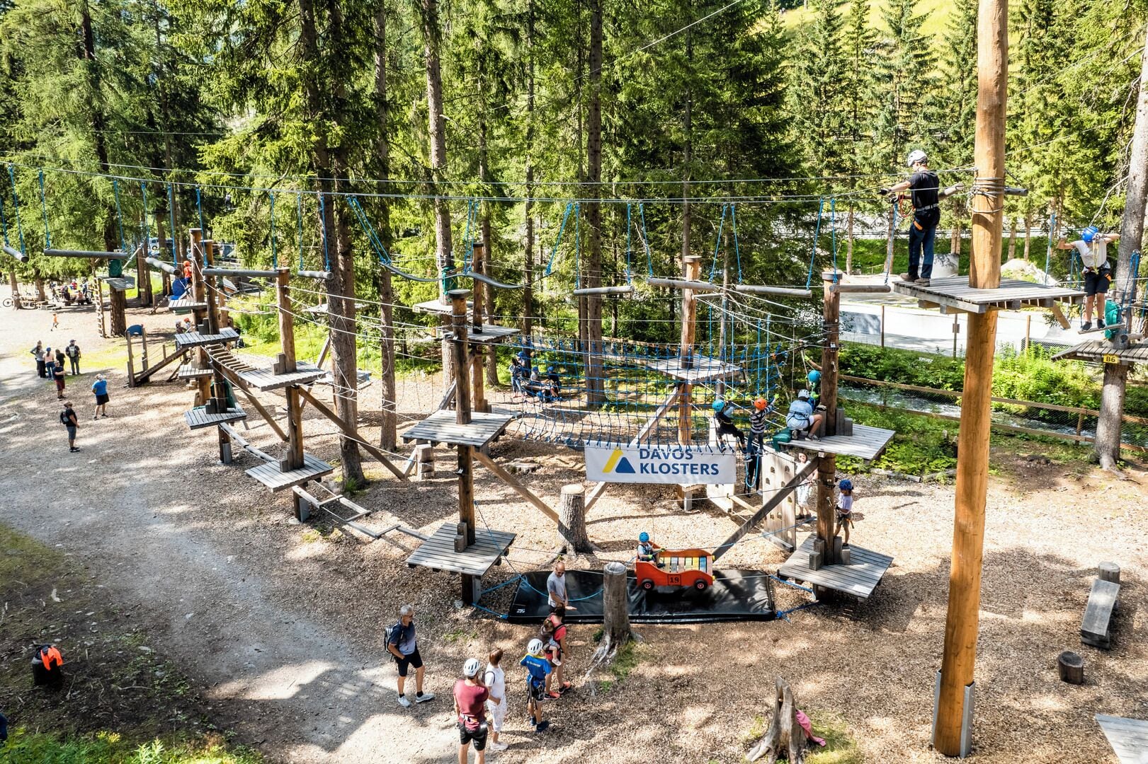 An outdoor adventure park with rope bridges, wooden platforms, and a sign for DAVOS KLOSTERS.